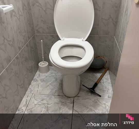 אסלה פתוחה עם מברשת שירותים וכלי עבודה על הרצפה